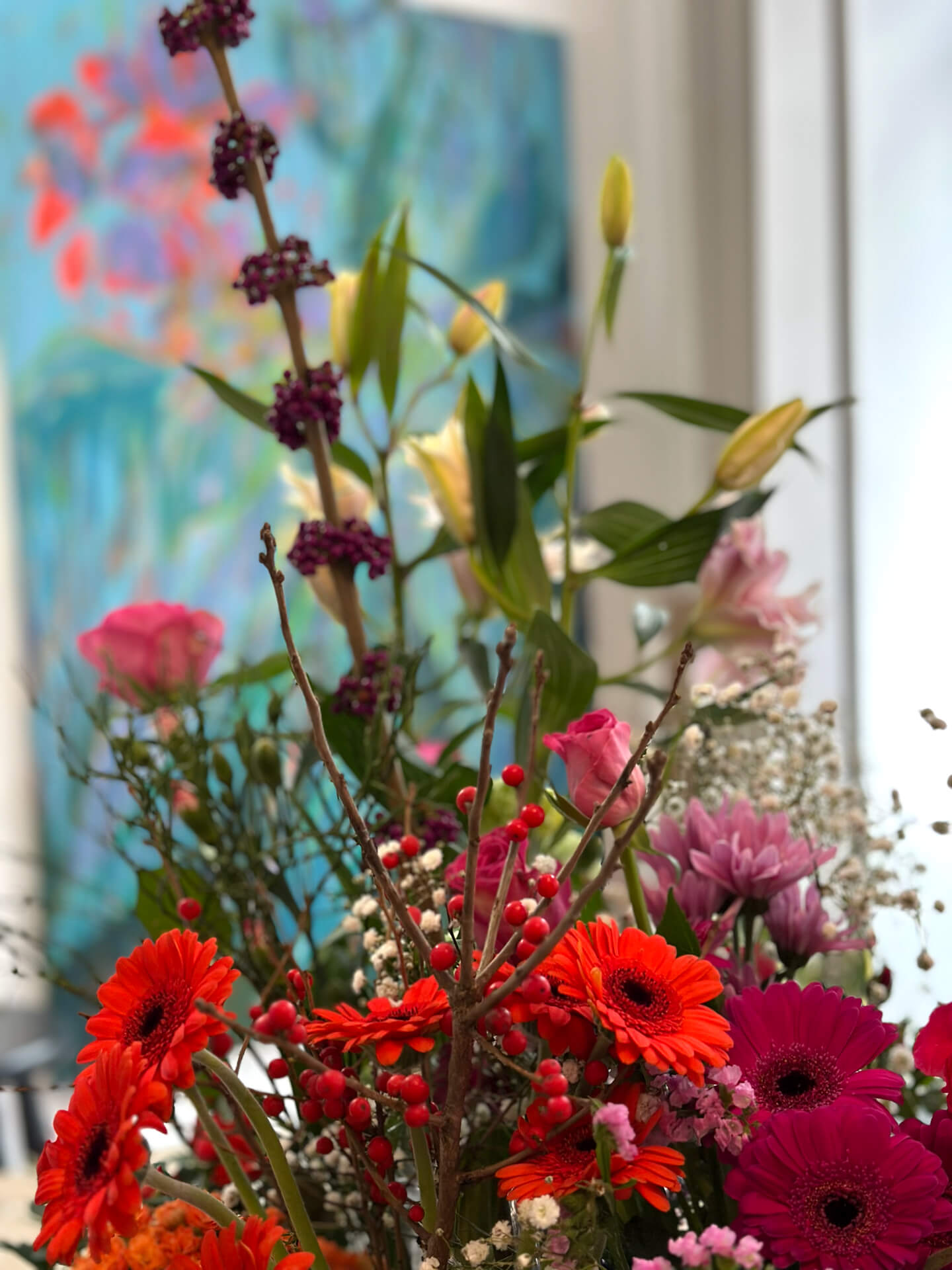 Farbenreiches Blumenarrangement vor einem großformatigen Gemälde im Atelier
